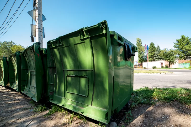Ряд зеленых мусорных контейнеров на обочине дороги под ясным небом