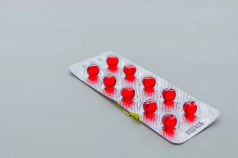 Упаковка красных капсул на сером фоне