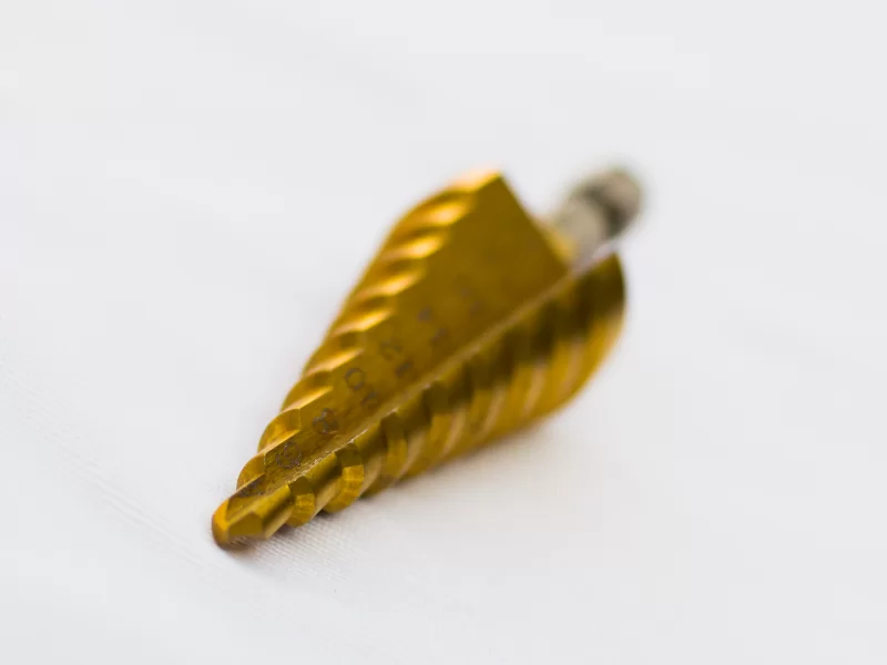 Золотая ступенчатая сверловая фреза на белом фоне