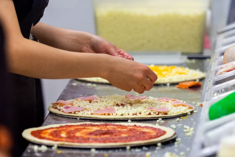 Процесс приготовления пиццы: повар добавляет ингредиенты на основу