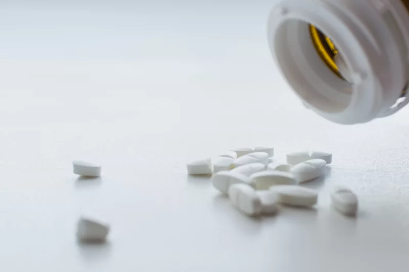 Белые таблетки, высыпающиеся из бутылки, крупный план