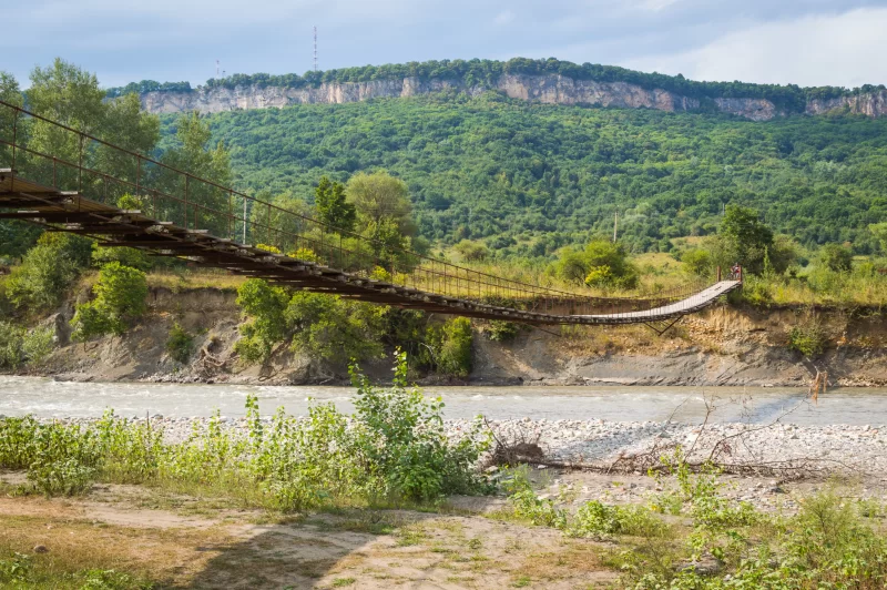 Старый подвесной мост над бурной горной рекой в живописном ущелье