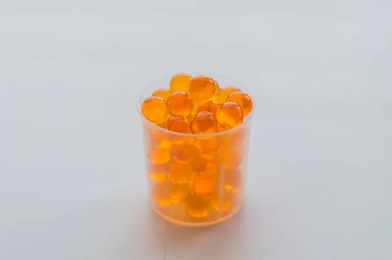 Яркие оранжевые капсулы в прозрачном стаканчике на светлом фоне