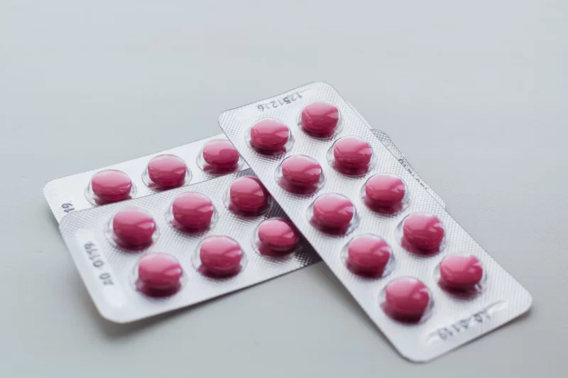 Две упаковки розовых таблеток на сером фоне