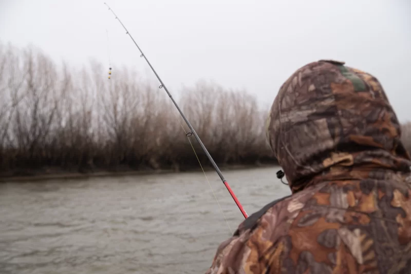 Fisherman in camouflage fishing on a river on a foggy day