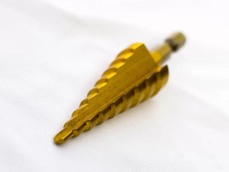 Золотая ступенчатая сверло для металла на белом фоне