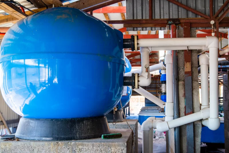 Большой синий расширительный бак с ПВХ-трубами