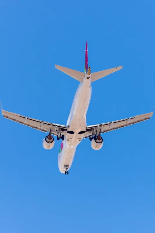 Белый самолет летит в чистом бледно-голубом небе.