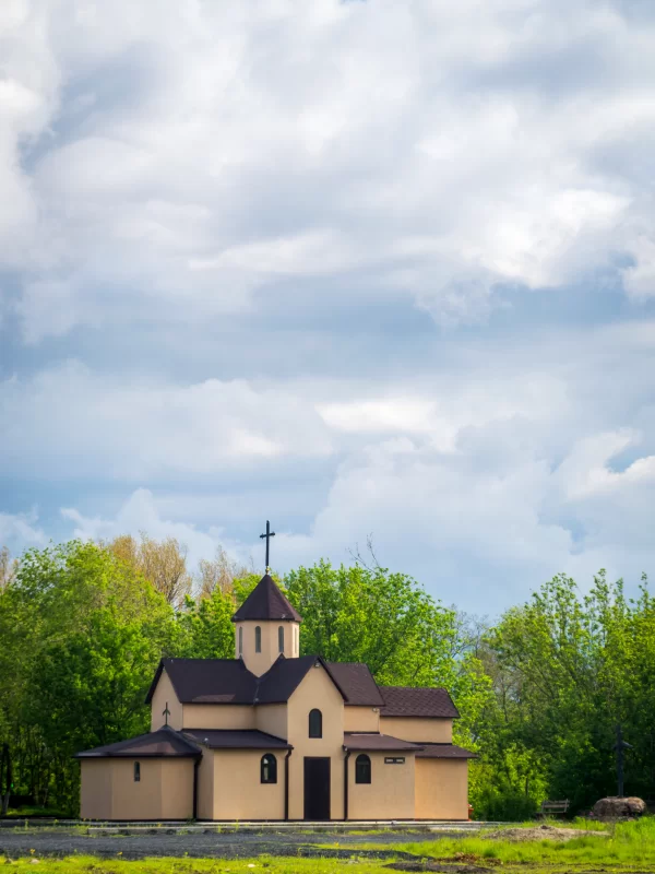 Небольшая церковь с крестом на фоне голубого неба и зелени