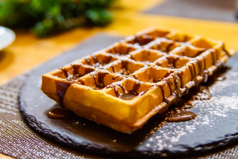 Аппетитный бельгийский вафель с шоколадом и сахарной пудрой на черной тарелке