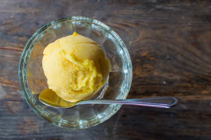 Яркий шарик лимонного мороженого в стеклянной креманке с ложкой на деревянном фоне