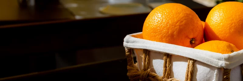 Сочные апельсины в плетеной корзине, освещенные солнцем