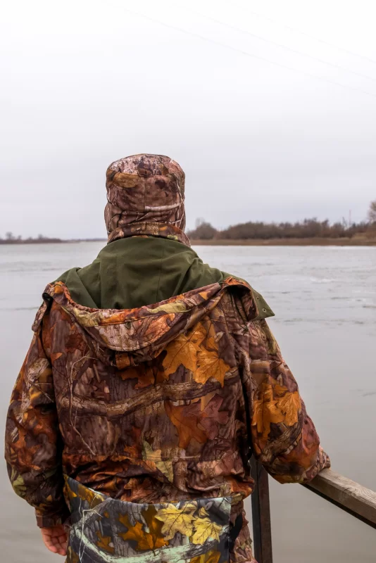 Охотник в камуфляже наблюдает за рекой в пасмурный день