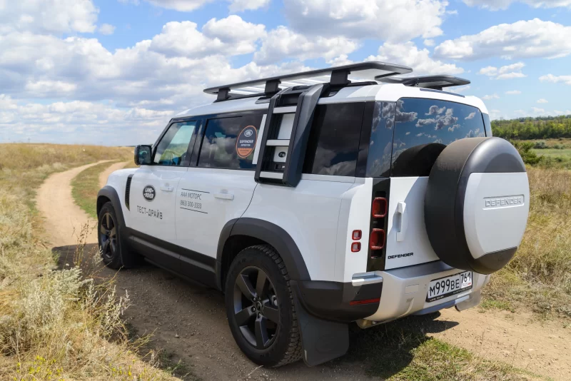 Белый Land Rover Defender на грунтовой дороге в поле