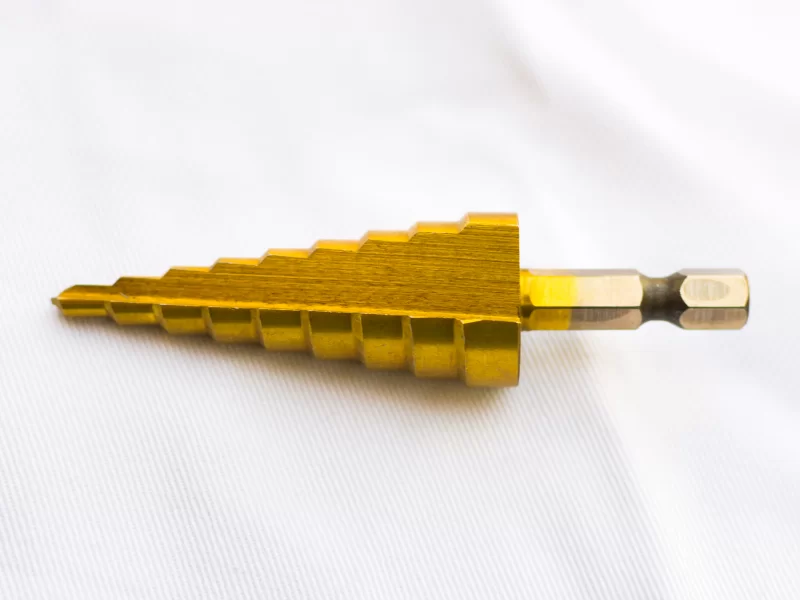 Золотая ступенчатая сверловая насадка для дрели на белом фоне