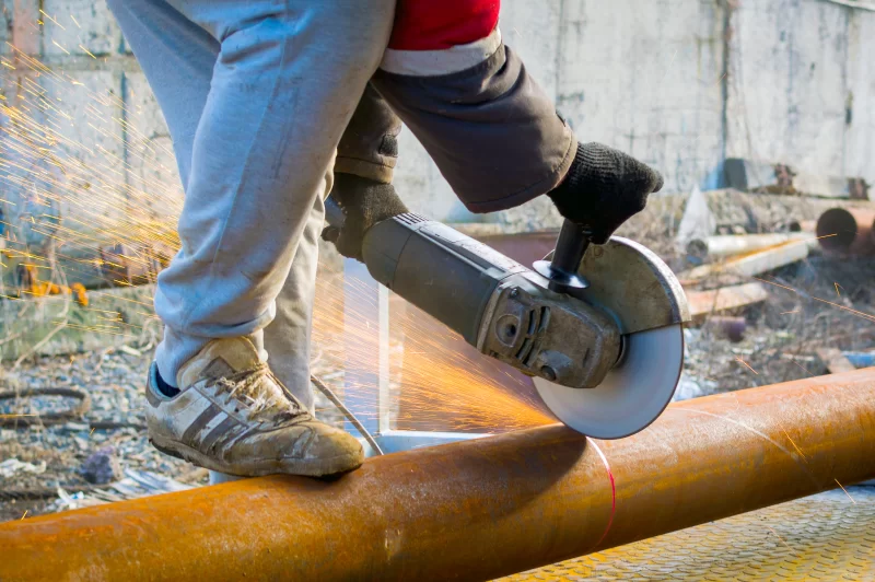 Рабочий использует угловую шлифовальную машину для резки металлической трубы, искры разлетаются