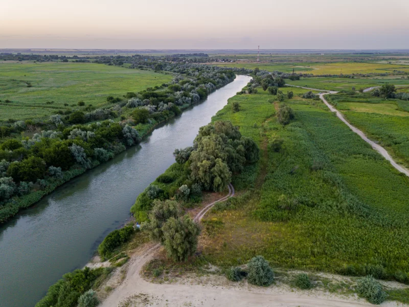 Спокойная река, извивающаяся сквозь зеленые поля и пышные деревья на закате