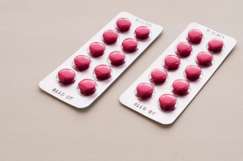 Две упаковки розовых таблеток в блистерах на светлом фоне