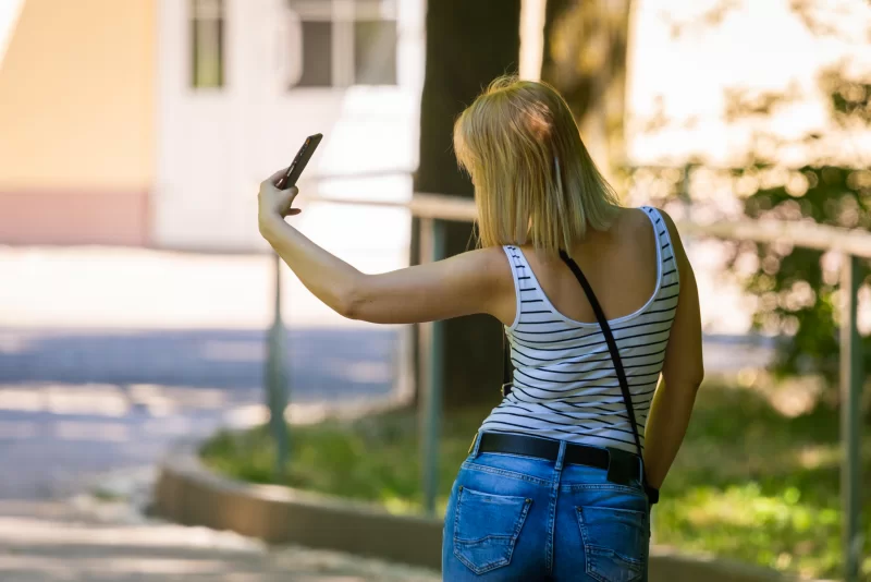 Девушка делает селфи на смартфон на фоне летнего парка