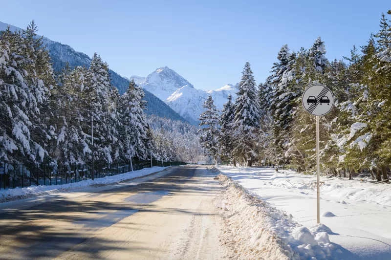 Зимний горный пейзаж с дорогой, заснеженными елями и знаком "Конец зоны обгона"