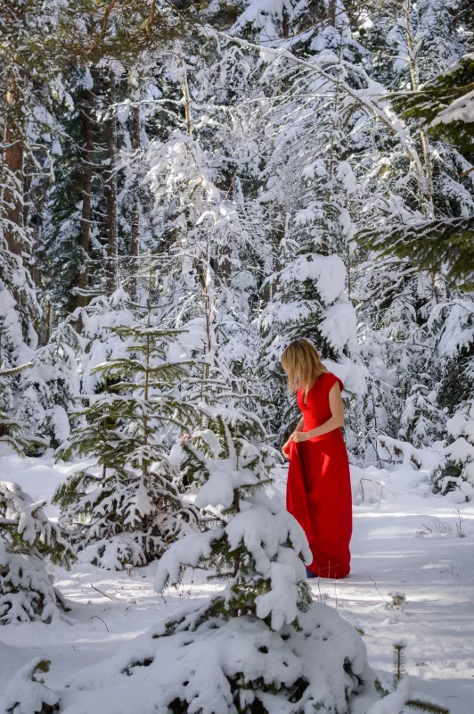 Elegant woman in a red dress among snowy fir trees