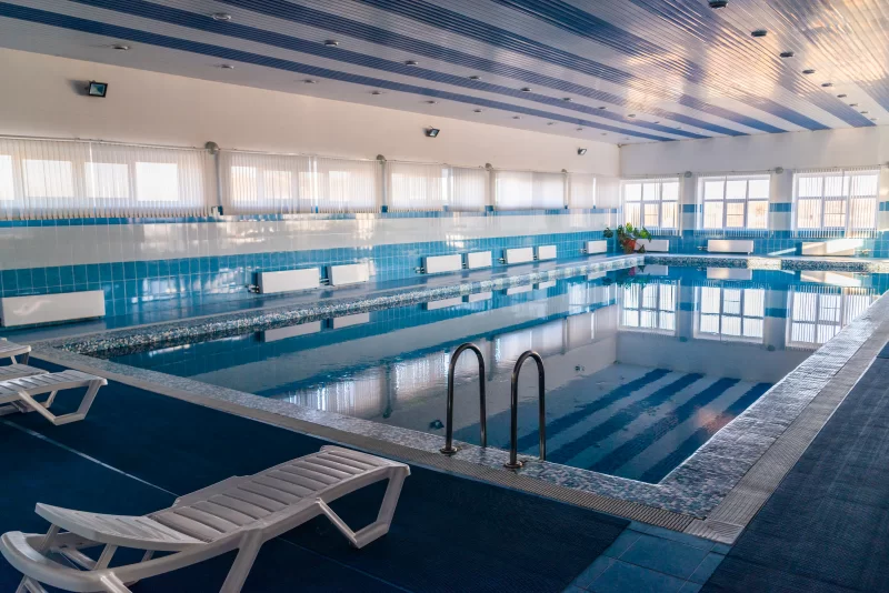 Современный крытый бассейн с голубой водой и шезлонгами