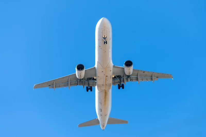 Белый самолет летит в чистом бледно-голубом небе.