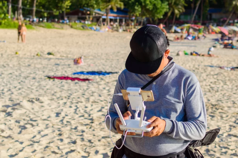 Оператор дрона управляет квадрокоптером на оживленном пляже