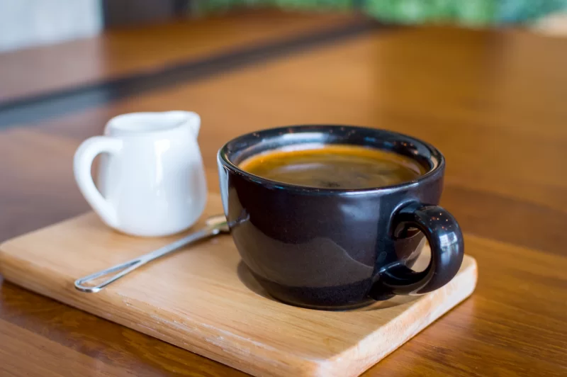 Чашка ароматного черного кофе и мини-сливочник на деревянной подставке