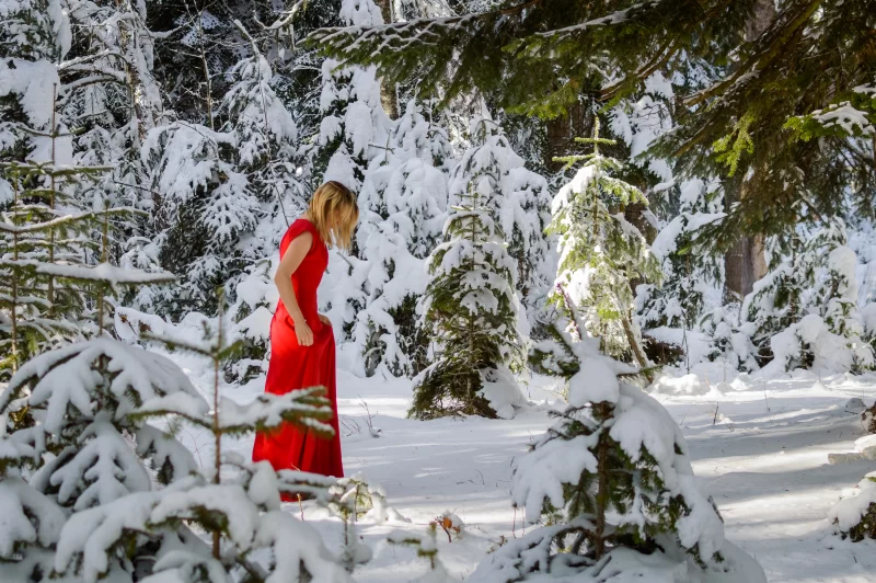 Elegant woman in red dress walking through a magical winter forest
